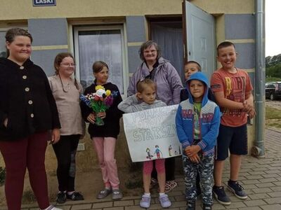 Wychowankowie z PWD z Lasek wręczają mieszkańcom Lasek kwiaty z krepiny i bibuły.