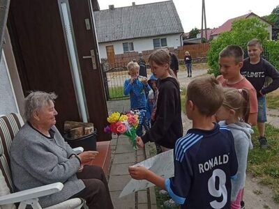 Wychowankowie z PWD z Lasek wręczają mieszkańcom Lasek kwiaty z krepiny i bibuły.