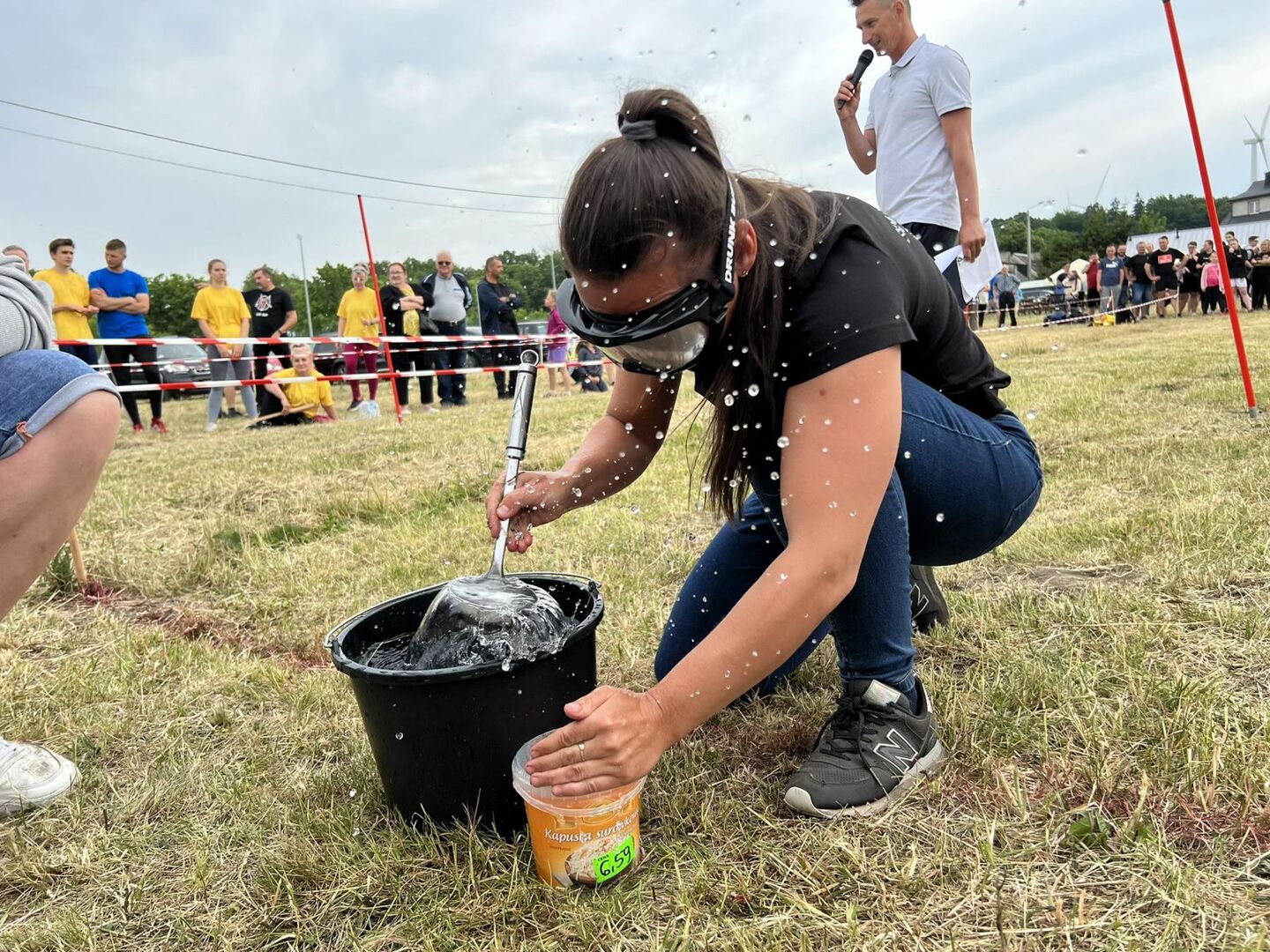 Uczestniczka potyczek za pomocą chochli przelewa wodę do wiaderka.