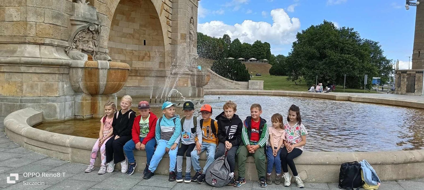 Dzieci pozują do zdjęcia przy fontannie.
