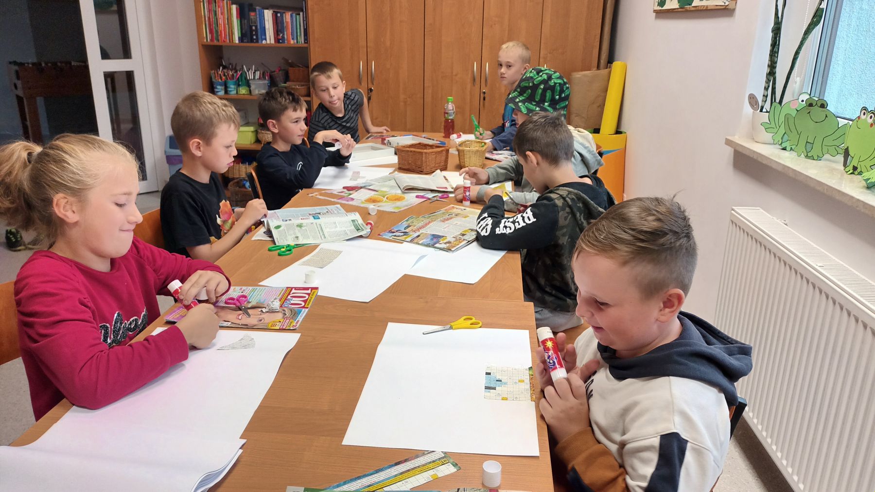 Dzieci wykonują kolaże z gazet przy użyciu pomocy dydaktycznych.