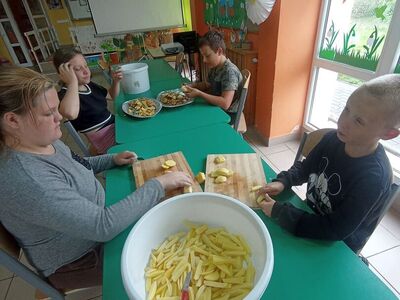 Wychowankowie z PWD z Lasek kroją ziemniaki na frytki.