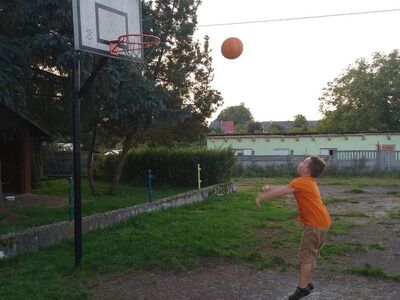 Chłopiec rzuca piłkę do kosza na boisku.