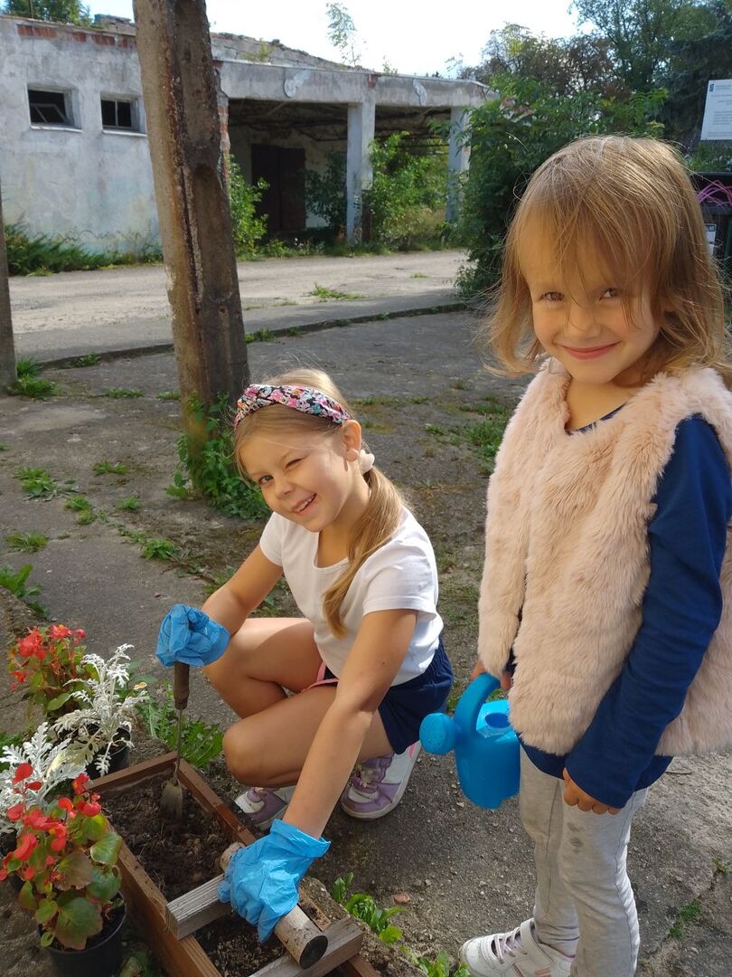 Dziewczynki pozują do zdjęcia podczas sadzenia kwiatów do skrzynki.
