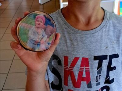 Chłopiec prezentuje portret na drewnianej deseczce wykonane techniką decoupage.