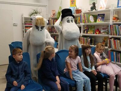 Dzieci siedzą na krzesłach. Za nimi - Muminki.