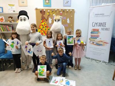 Dzieci pozują do zdjęcia z żywymi maskotkami - Muminkami i prezentują prace plastyczne.