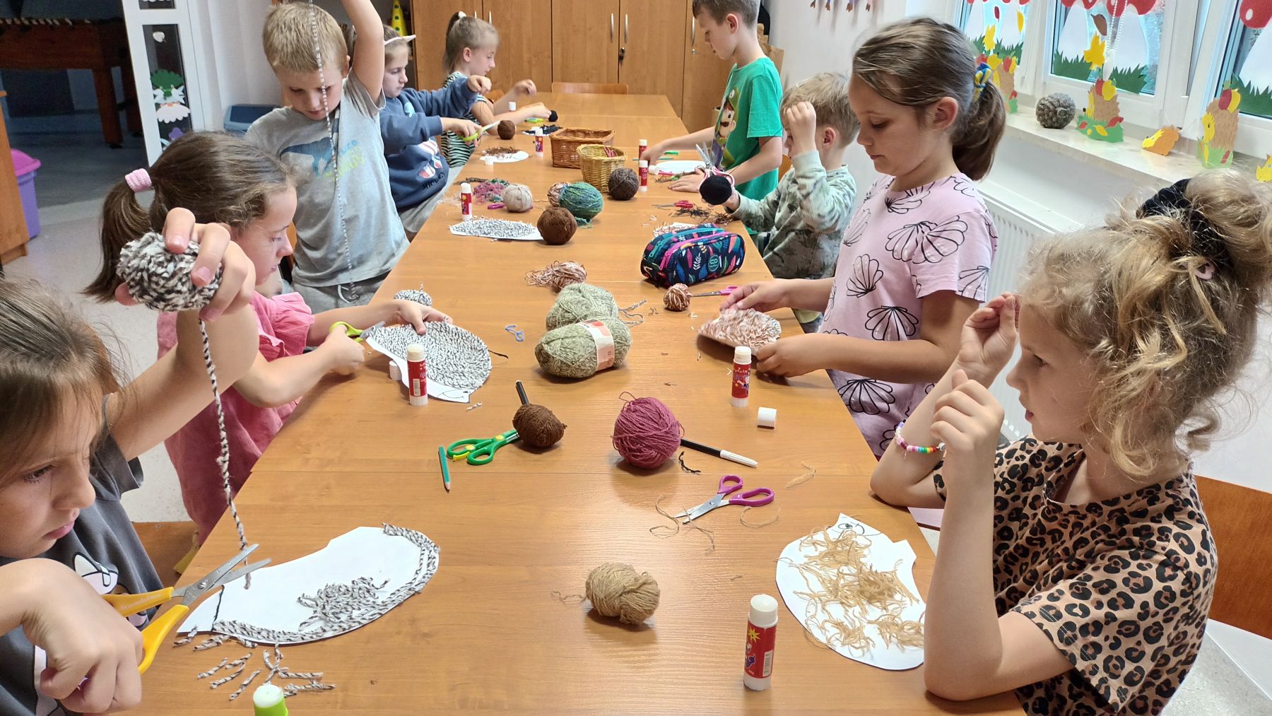 Dzieci przy użyciu włóczki ozdabiają jeżyki.