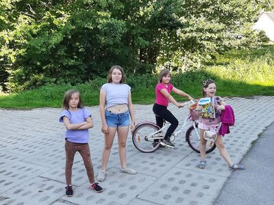 Dziewczynki pozują do zdjęcia na świeżym powietrzu. Dziewczynka w czerwonej koszulce na rowerze.