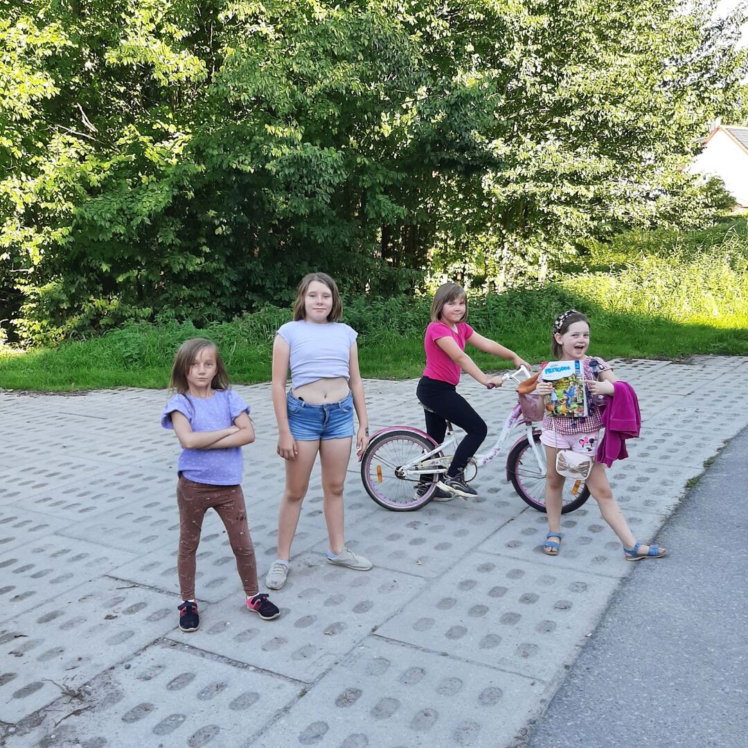 Dziewczynki pozują do zdjęcia na świeżym powietrzu. Dziewczynka w czerwonej koszulce na rowerze.