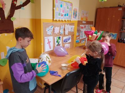 Chłopiec nadmuchuje balon. Dzieci przyklejają kolorowe bibuły na balon.