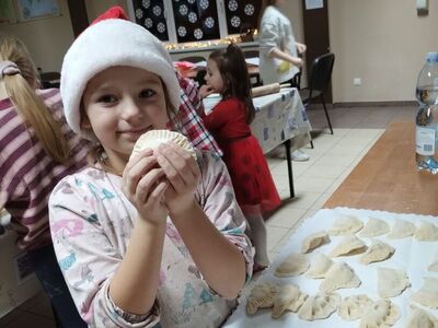 Dziewczynka w czapce mikołaja prezentuje  wykonane pierogi.
