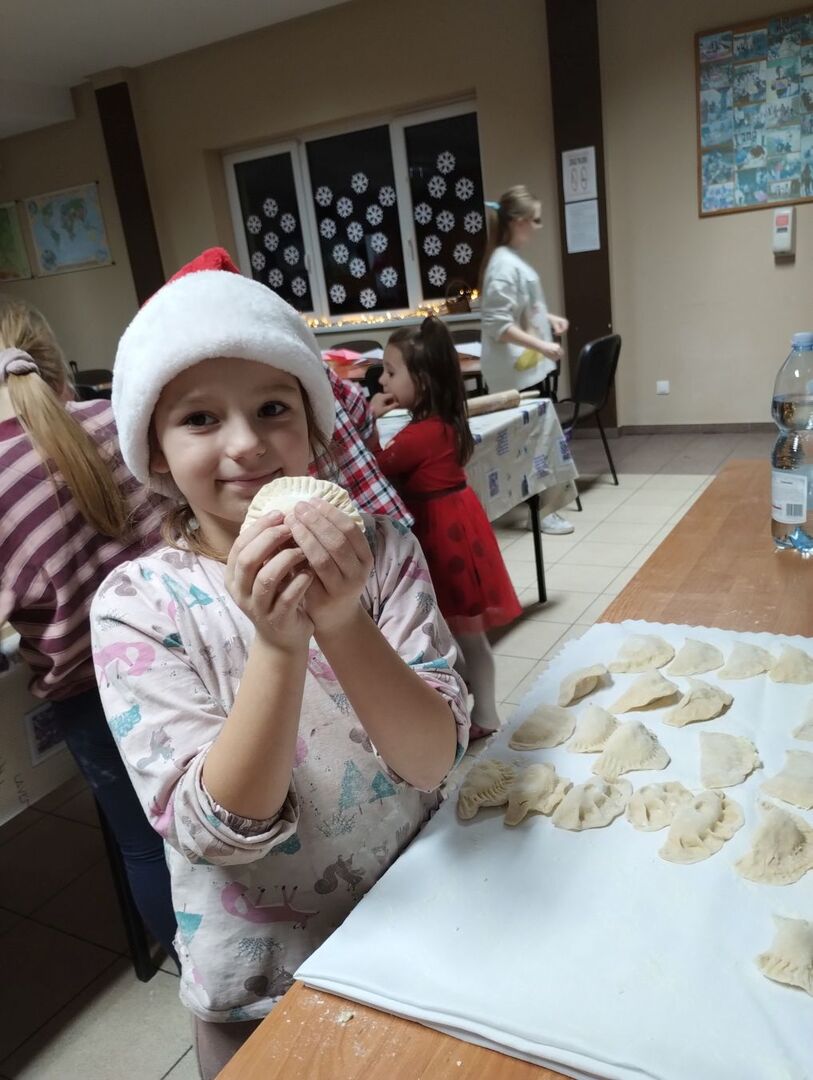 Dziewczynka w czapce mikołaja prezentuje  wykonane pierogi.