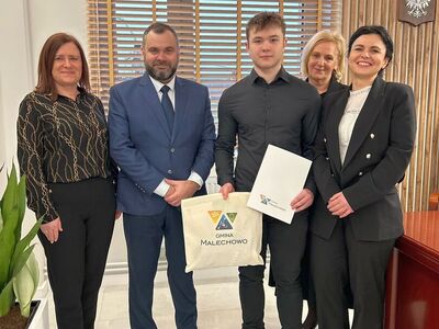 Nagrodzony sportowiec Bartłomiej Podbereżny w gabinecie wójta Radosława Nowakowskiego, przyjmuje od niego gratulacje. Towarzyszą mu: kierownik Referatu Oświaty i Sportu - Karolina Chruszcz-Pietraszewska, zastępca wójta - Halina Skaza i mama sportowca - Monika Podbereżna. 