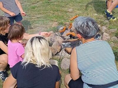 Dzieci pieką kiełbasy przy ognisku.