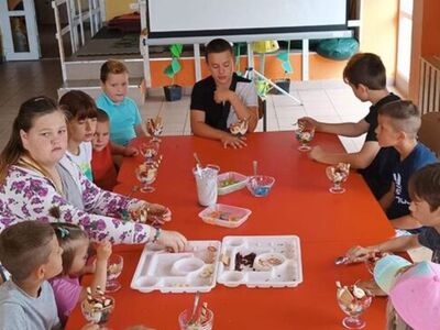 Dzieci dekorują desery z galaretką i bitą śmietaną. 