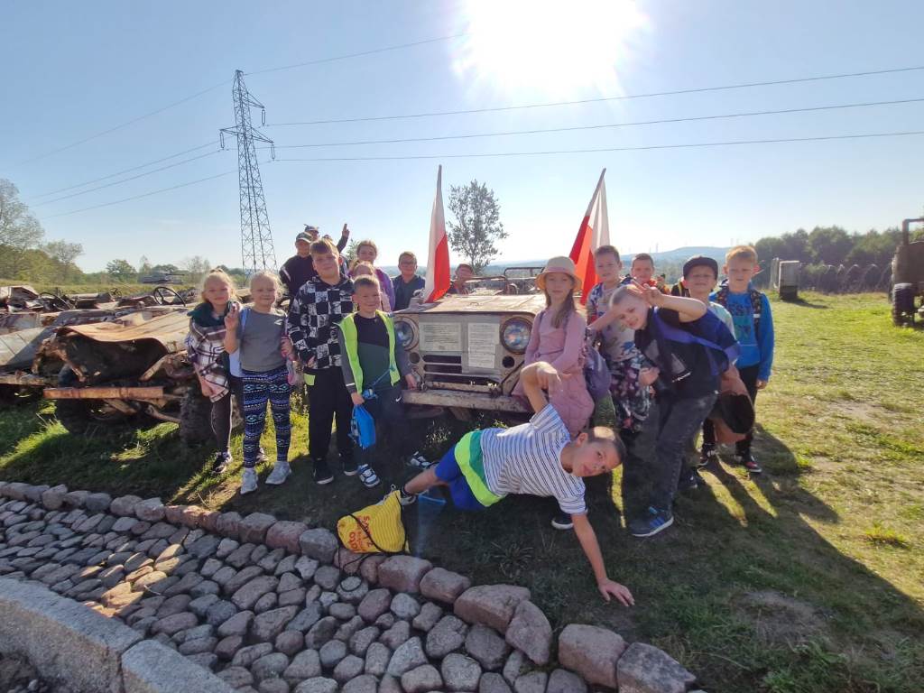 Pamiątkowe zdjęcie na tle pojazdu wojskowego z flagami Polski.