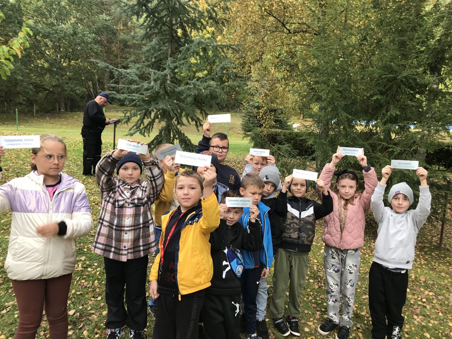 Uczniowie III klasy z tabliczkami opisującymi drzewa w szkolnym arboretum.