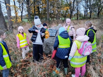 Dzieci zapalające znicze pod tablicą upamiętniającą dawnych mieszkańców tych terenów
