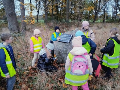 Dzieci zapalające znicze pod tablicą upamiętniającą dawnych mieszkańców tych terenów