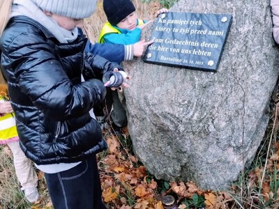 Dzieci zapalające znicze pod tablicą upamiętniającą dawnych mieszkańców tych terenów