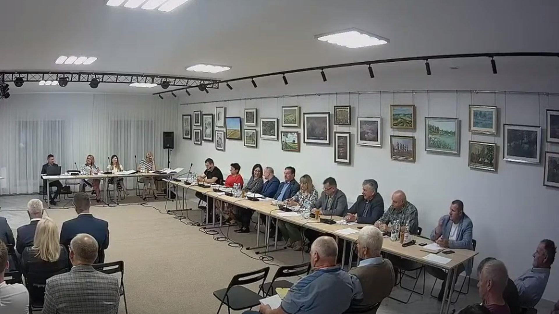 Zdjęcia przedstawiające obrady sesji. Przedstawia osoby siedzące za stolami obrad.
