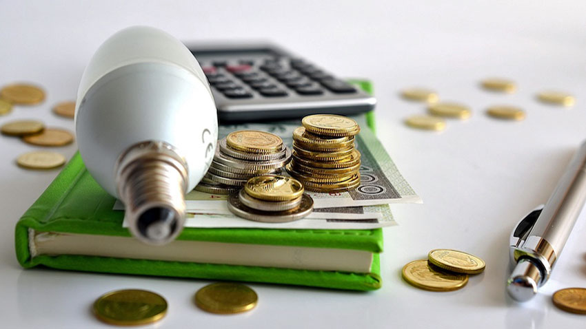 Na zdjęciu widnieje żarówka, pieniądze, kalkulator. 
Źródło zdjęcia: https://bank.pl/ceny-energii-gdzie-na-fakturze-ukryta-jest-nasza-podwyzka/