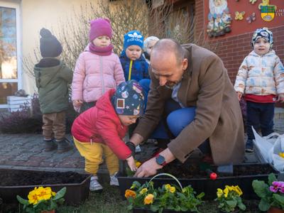 Na zdjęciu Zastępca Burmistrza Tychowa Jacek Marcinkowski pomaga sadzić maluszką ze złobka kwiaty.