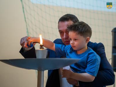 Na zdjęciu Burmistrz Tychowa Robert Falana wraz przedszkolakiem odpalają symboliczny płomień na znak rozpoczęcia III Niebieskich Igrzysk.