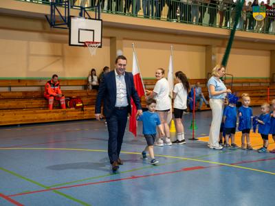 Zdjęcie wykonanane podczas III Niebieskich Igrzysk. Na zdjęciu chłopiec ubrany w niebieską koszulkę prowadzi Burmistrza Tychowa do odpalenia symbolicznego płomienia.