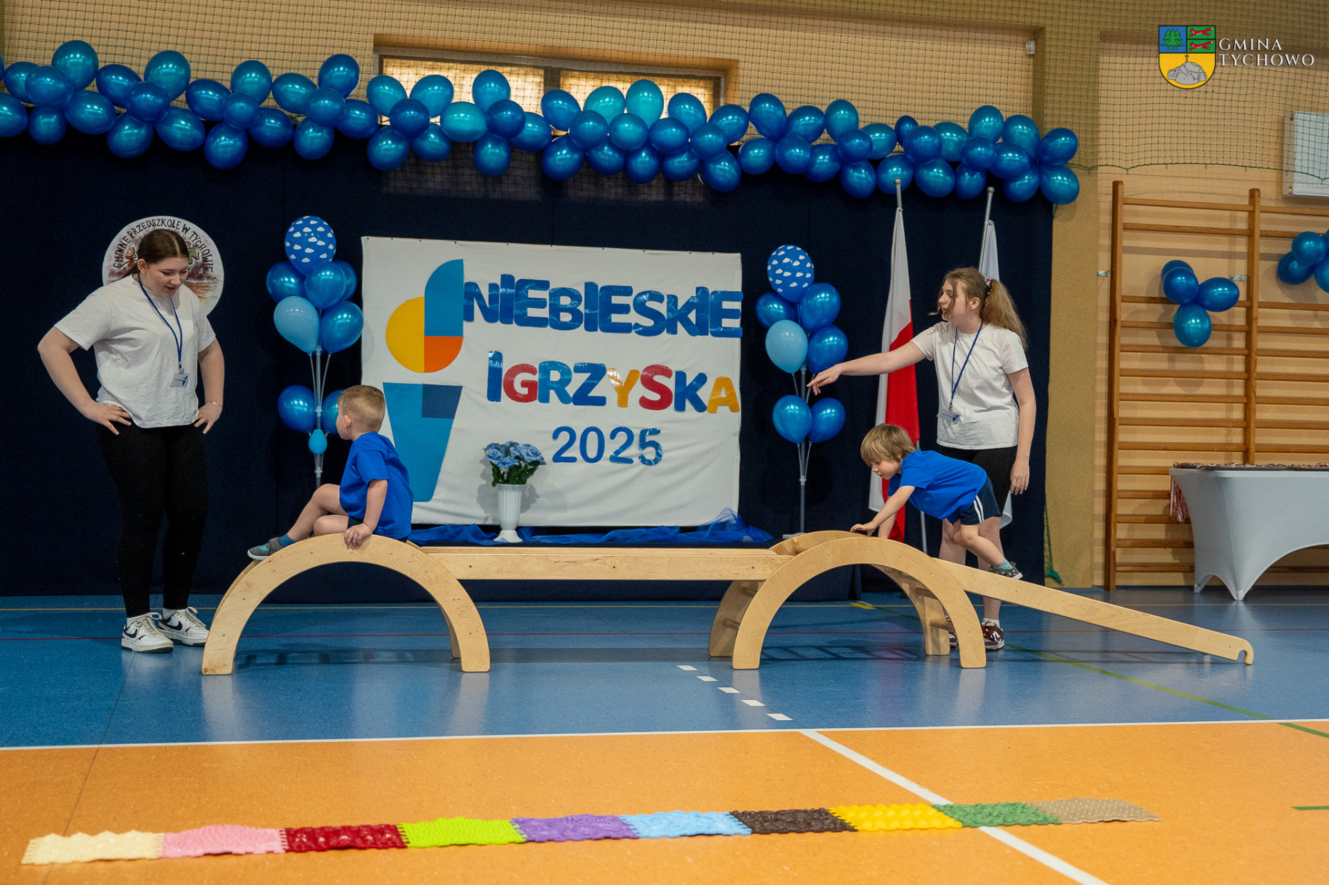 Zdjęcie wykonanane podczas III Niebieskich Igrzysk. Na zdjęciu znajdują się dzieci ubrane w niebieskie koszulki biorące udział w igrzyskach oraz uczennice Szkoły Podstawowej w Tychowie.