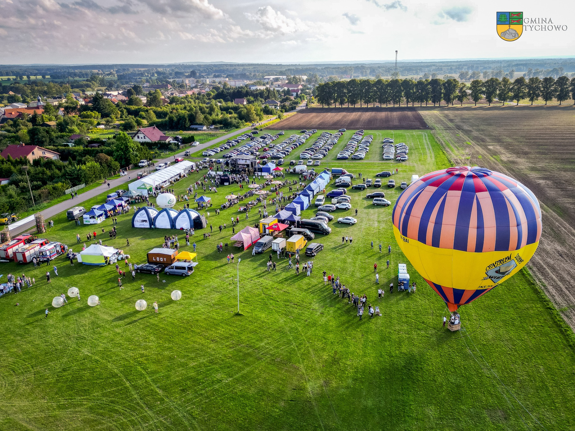 Na zdjęciu widok z drona na imprezę "Dożynki Gminne w Tychowie". Na zdjęciu widać scenę, wystawców, stoiska sołeckie oraz balon.