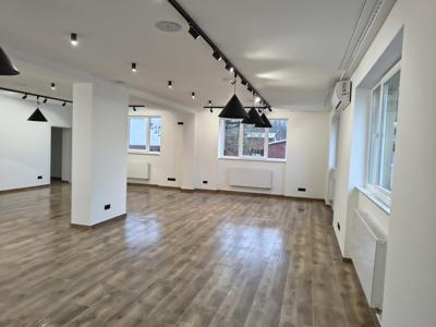 Na zdjęciu sala wystawowa pomalowana na biało z ułożonymi płytkami na podłodze i zamontowanymi szynami oświetleniowymi, wystawowymi i nagłośnieniem. Na zdjęciu widać okna i grzejniki.