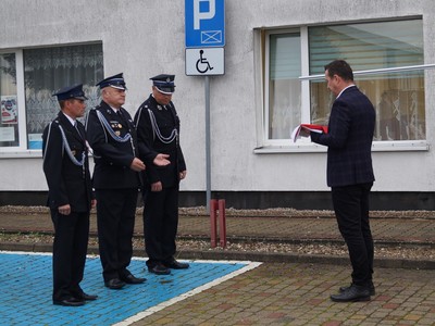 zdjęcie przedstawia Druhów Ochotniczej Straży Pożarnej w Tychowie przyjmujących od burmistrza Tychowa Roberta Falany flagę Rzeczpospolitej Polski do zawieszenia na maszcie przed Urzędem Miejskim